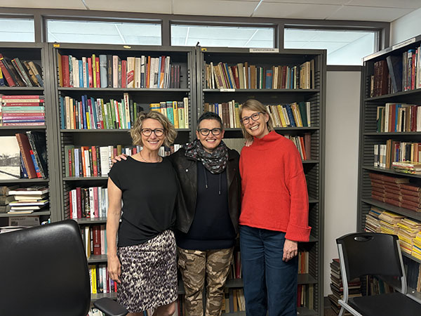three woman smiling in fron tof book case